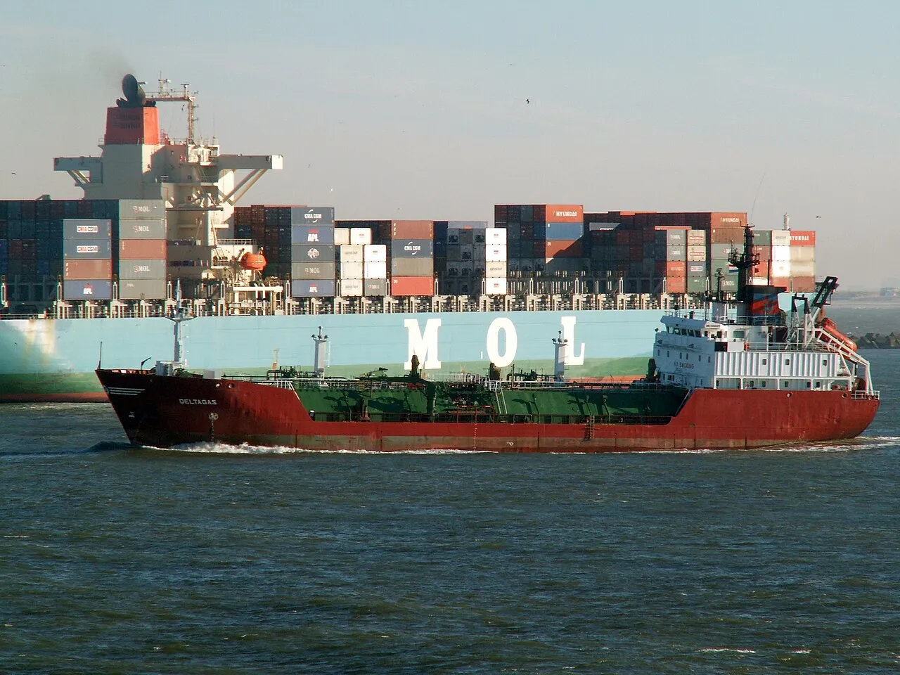 A red gas tanker turning in front of a fully loaded container ship